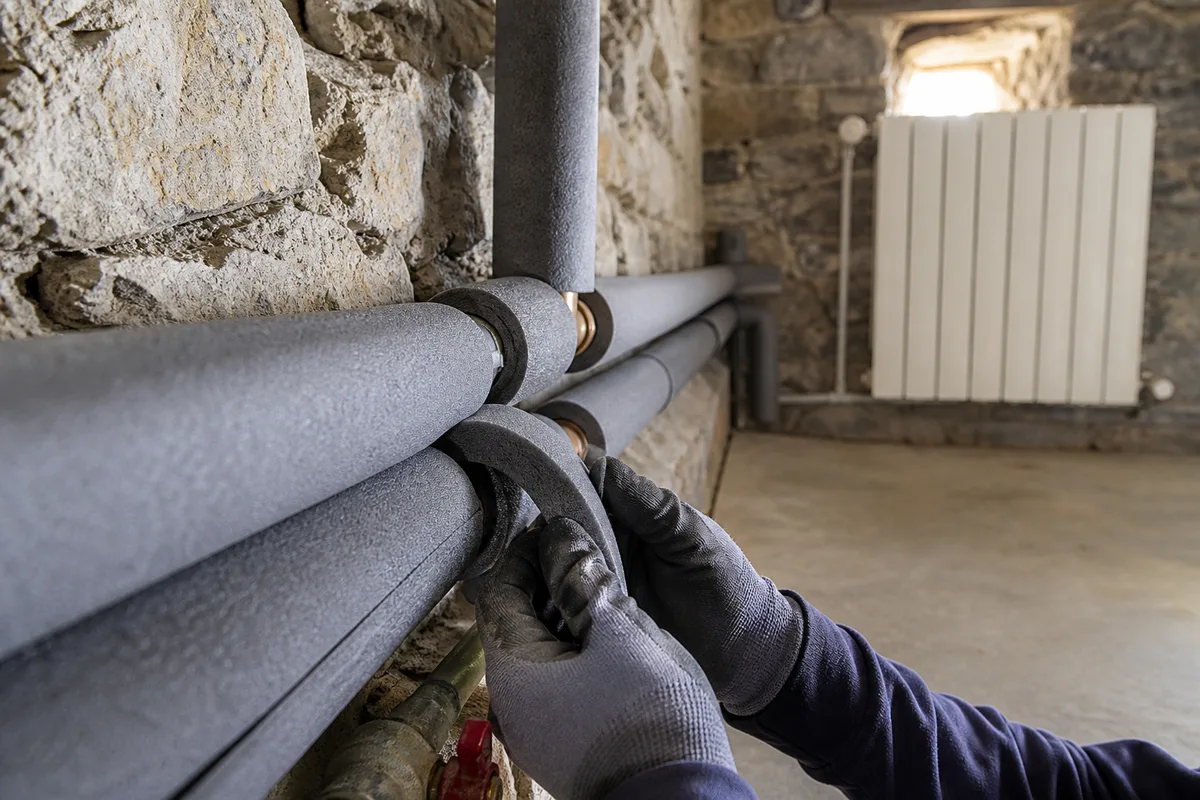 Radiateur et tuyaux calorifugés dans un vide sanitaire de chalet savoyard, lumière froide