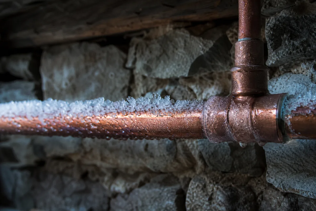 Canalisation givrée en sous-sol d’un chalet savoyard, lumière froide de fin de journée