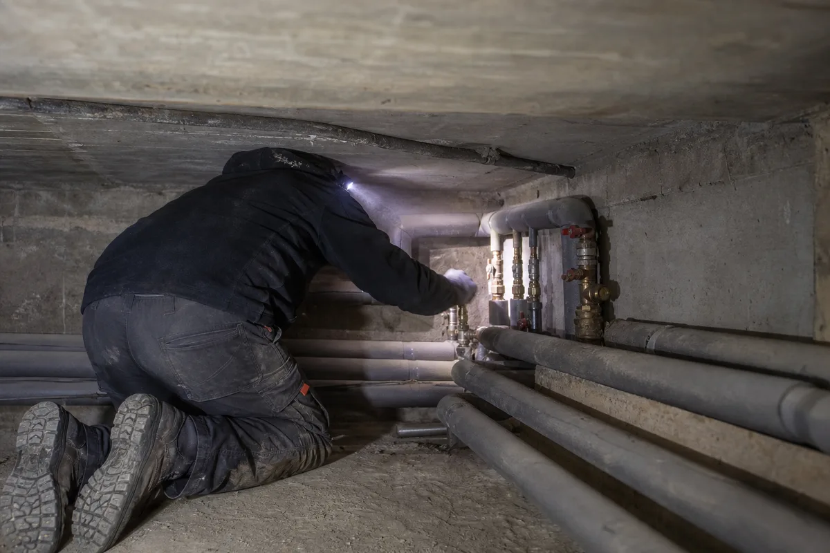 Silhouette d’artisan de dos réglant une vanne sur un réseau de chauffage en vide sanitaire